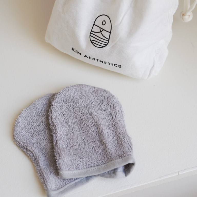 An eco-friendly 20-pack of reusable bamboo facial mitts arranged on a clean bathroom counter next to a skincare routine cleanser, perfect for a sustainable clinic-at-home experience.