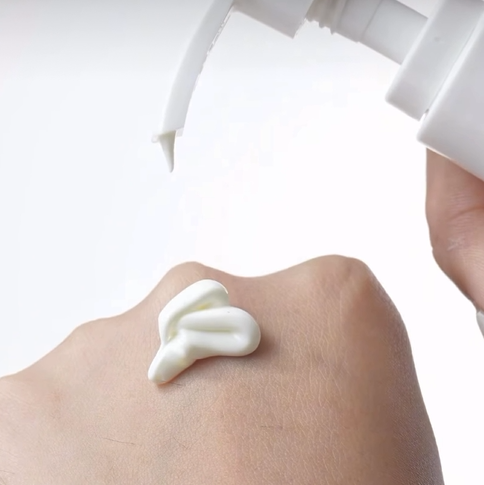 The silky, fast-absorbing texture of Body Factorie Body Shield being dispensed, showing a non-greasy Korean sunscreen formula that hydrates with an 8-form Hyaluronic Acid complex.