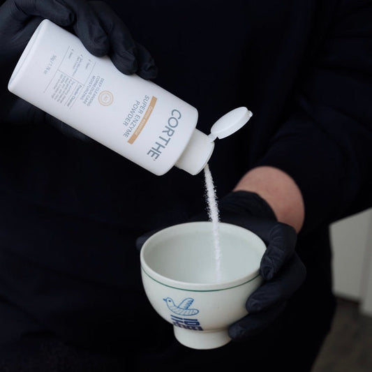 Dispensing Corthe Korean Enzyme Powder into a treatment bowl, showing the fine-grained exfoliating powder that activates with water for a non-abrasive facial cleanse.