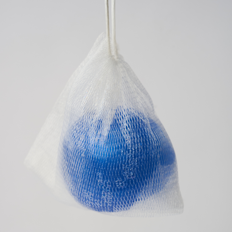 The deep blue Bouncy Ball Soap with Azulene in a foaming mesh bag; A playful, bouncy texture and a five-peptide complex that firms and renews body skin.