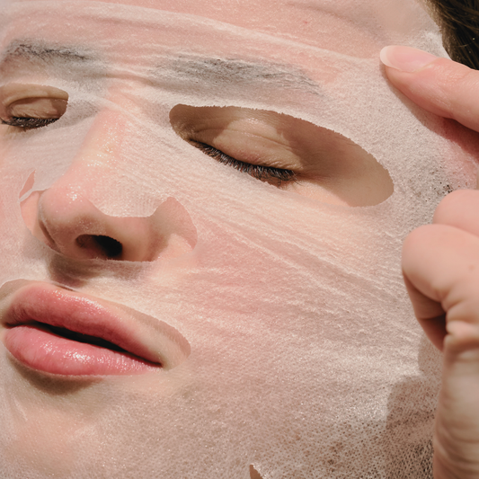 Close-up of the high-adhesion Corthe sheet mask being applied to the forehead and eye area, showing the thin, bio-active essence-soaked material that delivers Madecassoside to calm inflamed skin.