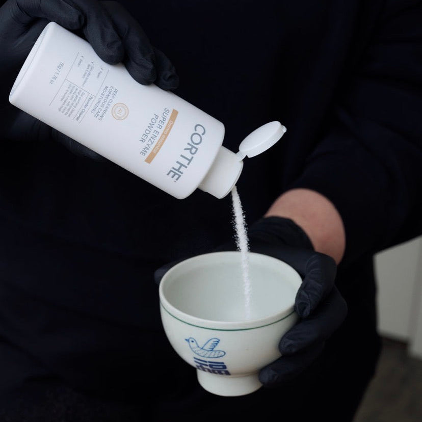 Dispensing Corthe Korean Enzyme Powder into a treatment bowl, showing the fine-grained exfoliating powder that activates with water for a non-abrasive facial cleanse.